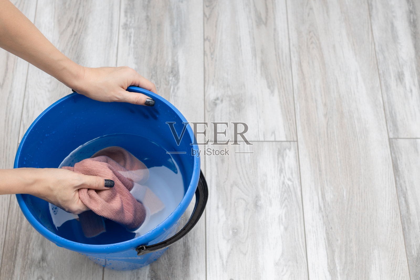 一名妇女在清洁时把抹布湿在桶里。照片摄影图片