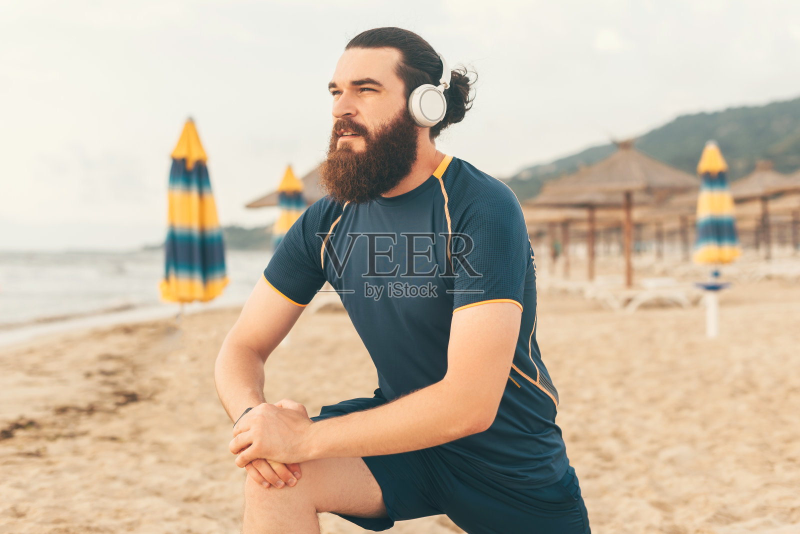 年轻的大胡子男子听音乐在他的耳机，同时做暖身前晨跑照片摄影图片