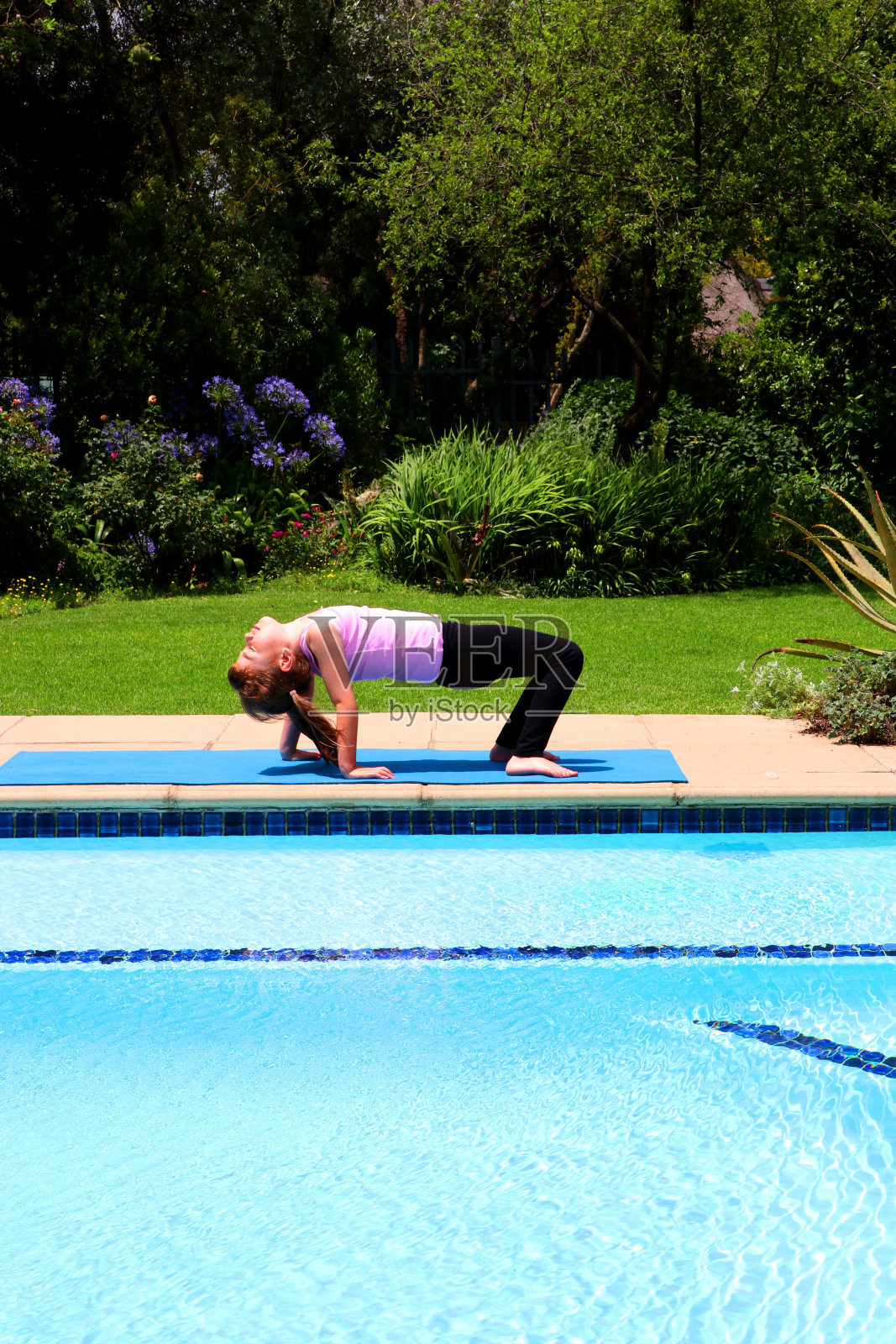 夏天，年轻的女孩在花园里做瑜伽，在一个蓝色的运动垫上，穿着粉红色的上衣，坐下来照片摄影图片