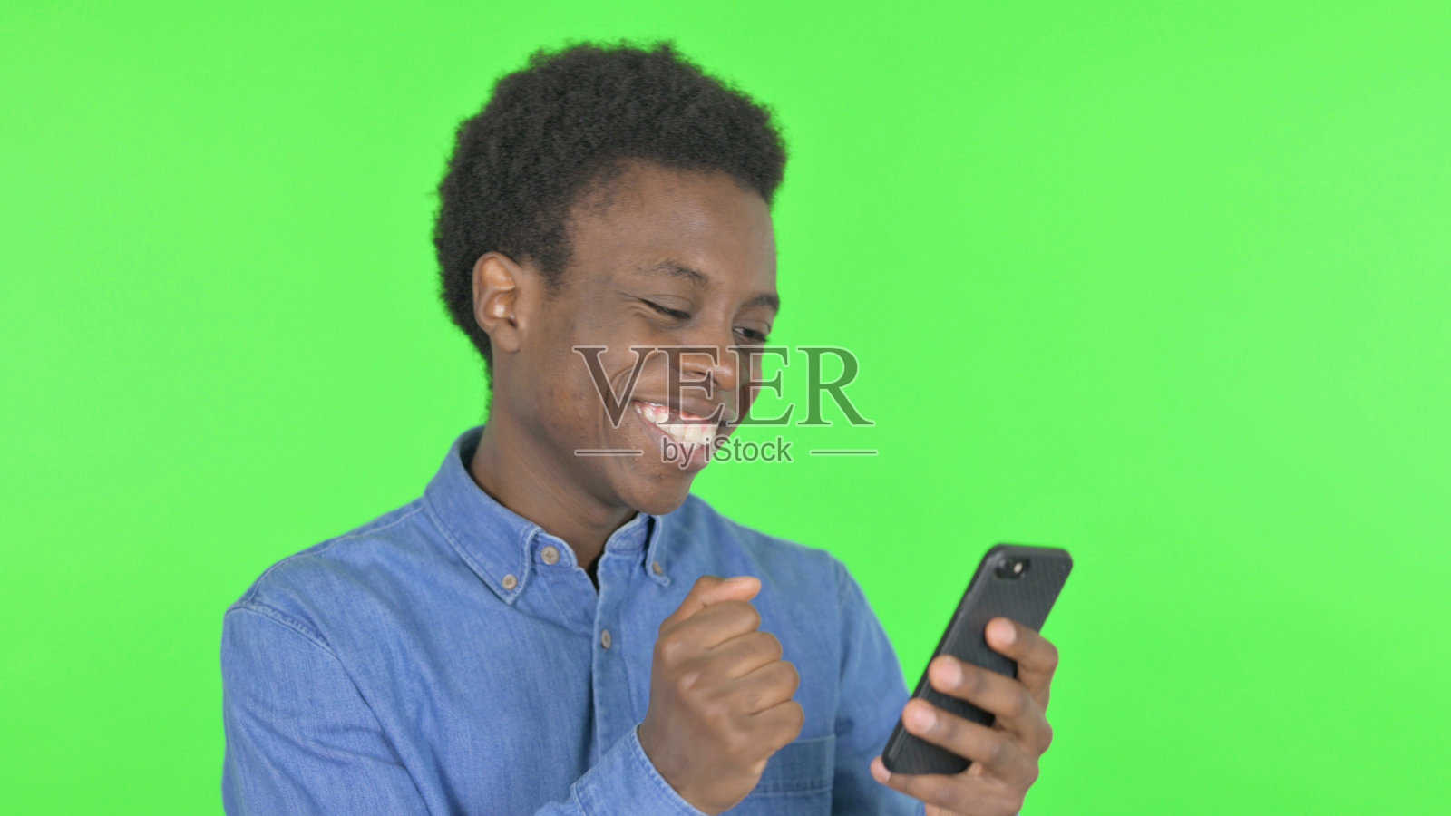 年轻的非洲男子在绿色背景的智能手机上庆祝照片摄影图片