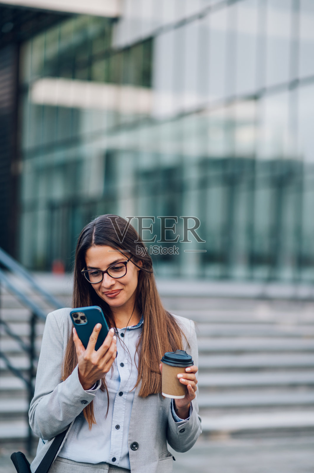 一位商务女士站在外面一边用智能手机一边喝咖啡照片摄影图片