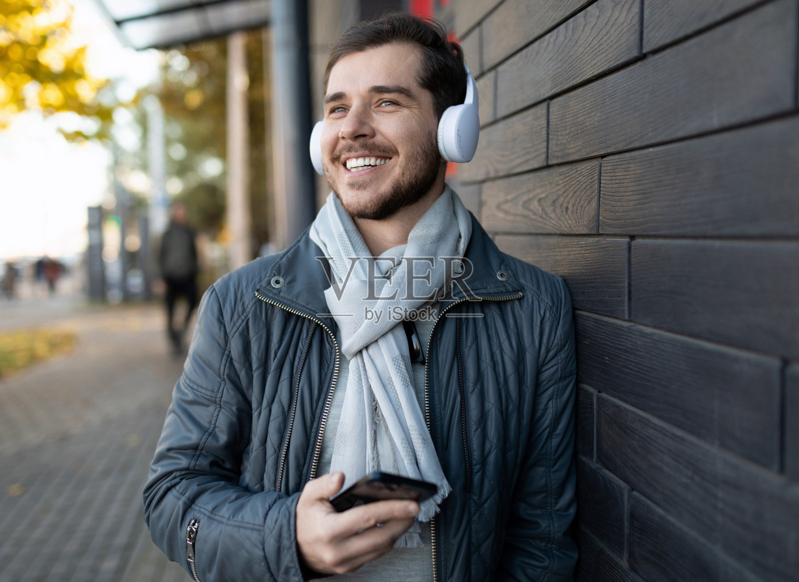 一名快乐的成年男子戴着白色耳机听着手机上的音乐，微笑着看着远方照片摄影图片
