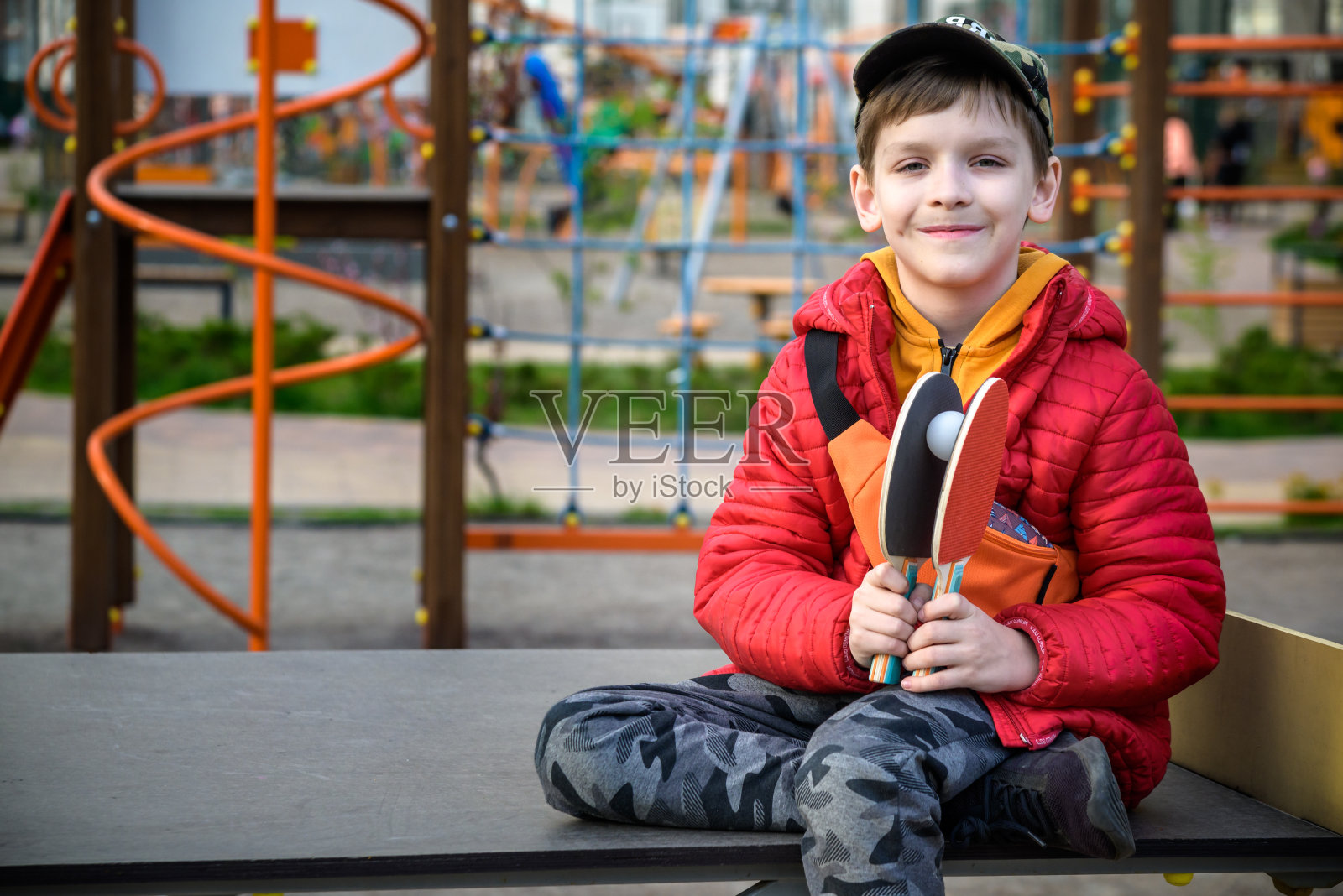 快乐的乒乓球运动员思考一场比赛。比赛结束后，小男孩坐在室外的网球桌上照片摄影图片