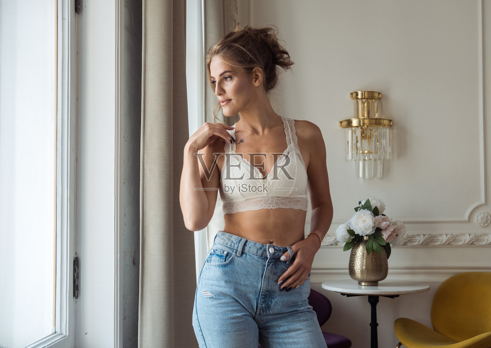 一个穿着牛仔裤和蕾丝上衣的迷人的金发女郎站在客厅里照片摄影图片