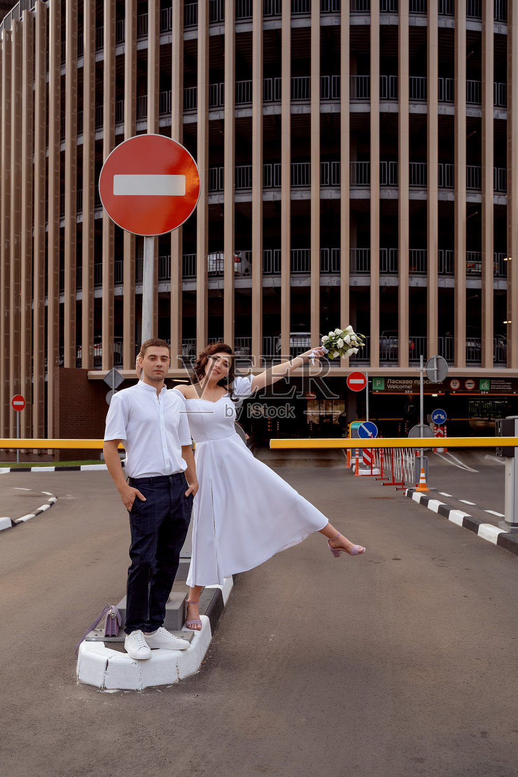 新娘和新郎挂在一个多层停车场入口附近的一个道路停车标志上。醉醺醺的新婚夫妇在城里打架。城市风格的婚礼。有选择性的重点照片摄影图片