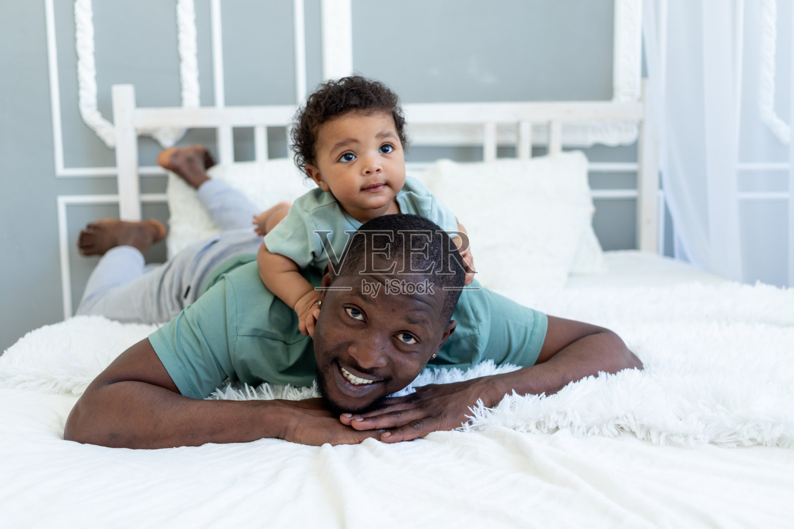 美国黑人爸爸在卧室的床上和儿子玩拨浪鼓，父亲的爱照片摄影图片