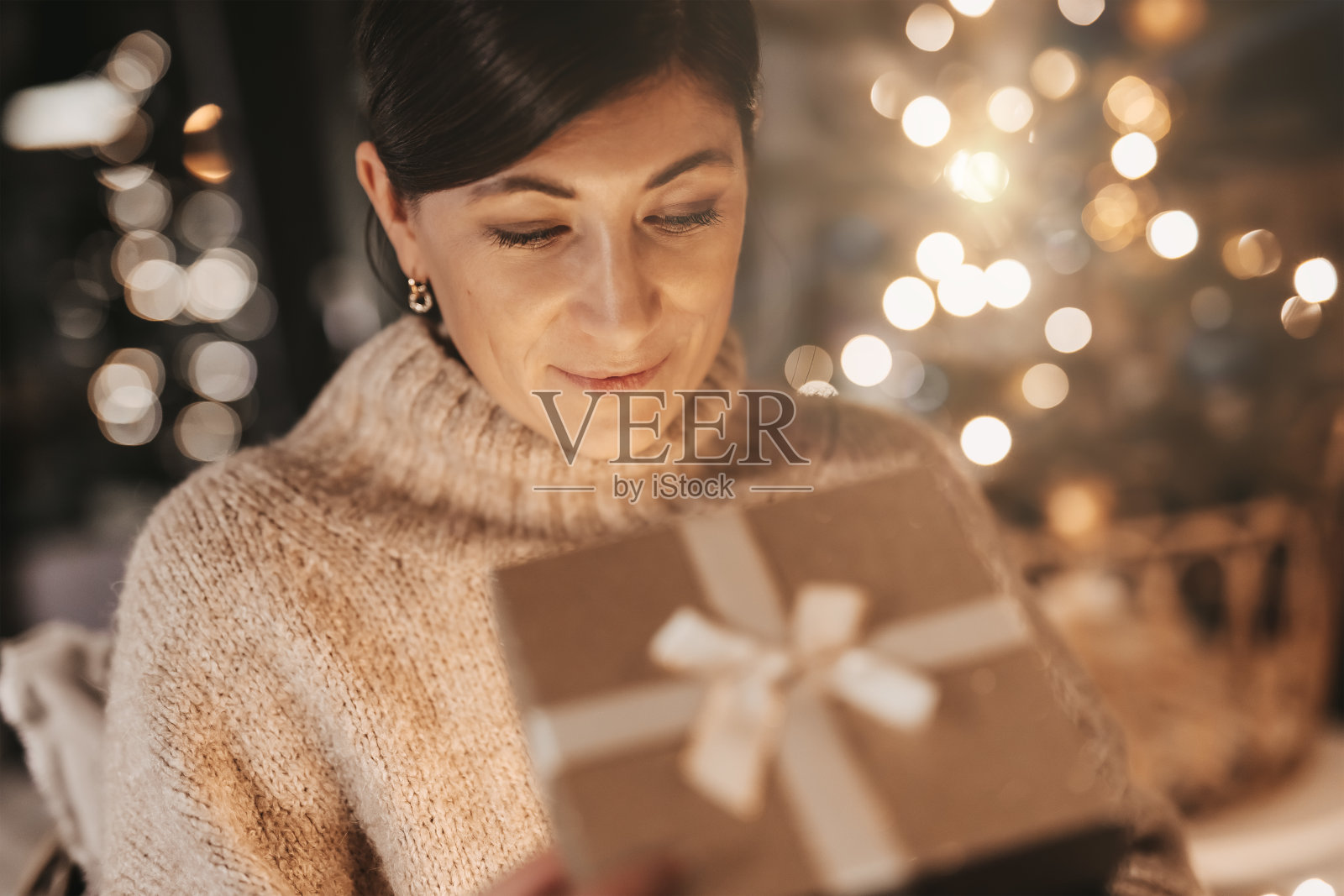 快乐的女人打开礼物，她兴奋地看着盒子，在一个舒适的环境在家里，神秘的，温暖的颜色照片摄影图片