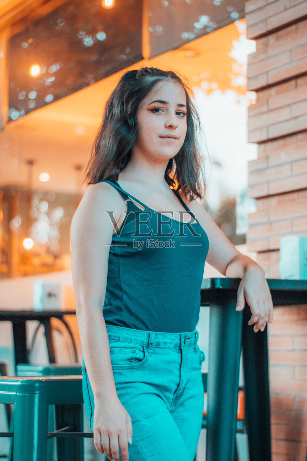 一个年轻的白人女孩，穿着黑色背心和牛仔裤，站在户外咖啡馆的椅子旁照片摄影图片