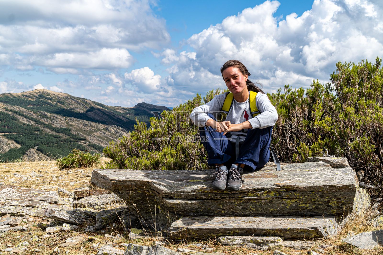 金发的西班牙女性，波浪形的头发，坐在一块岩石上，休息在一个山徒步路线照片摄影图片