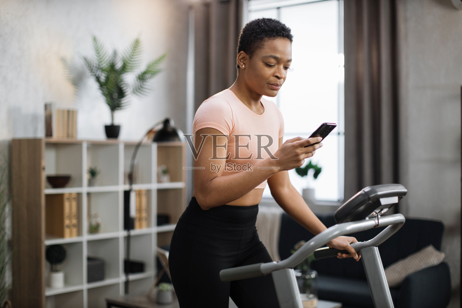 活跃的非洲妇女肖像在运动服使用智能手机，跑步机使用跑步机照片摄影图片