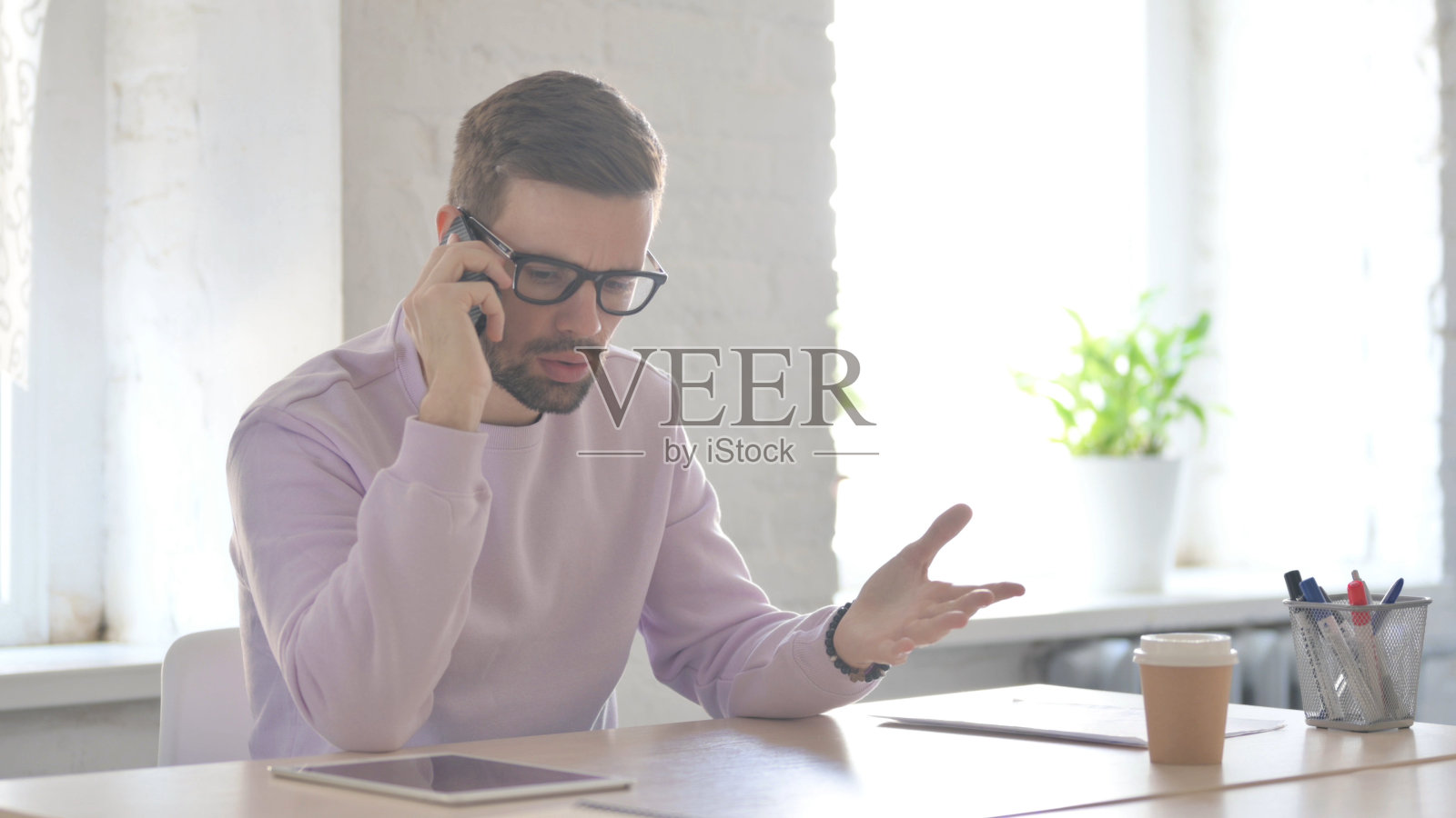 心烦意乱的年轻人在办公室用智能手机生气地说话照片摄影图片