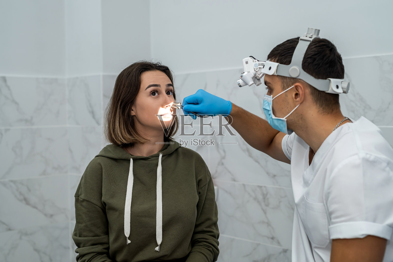 一名男性耳鼻喉科医生在鼻内窥镜检查前检查一名女性患者的鼻子照片摄影图片