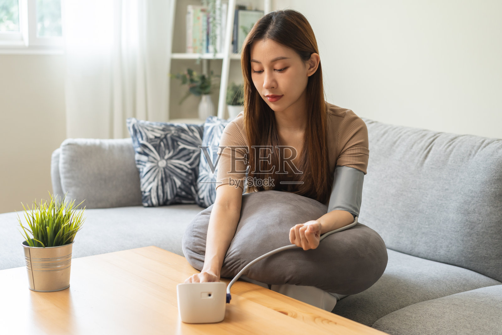 低血压，亚洲年轻女性坐在沙发上用数字压力监测器检查血压、血压和心率，在家对她的手臂进行自我检查。保健和医疗。照片摄影图片