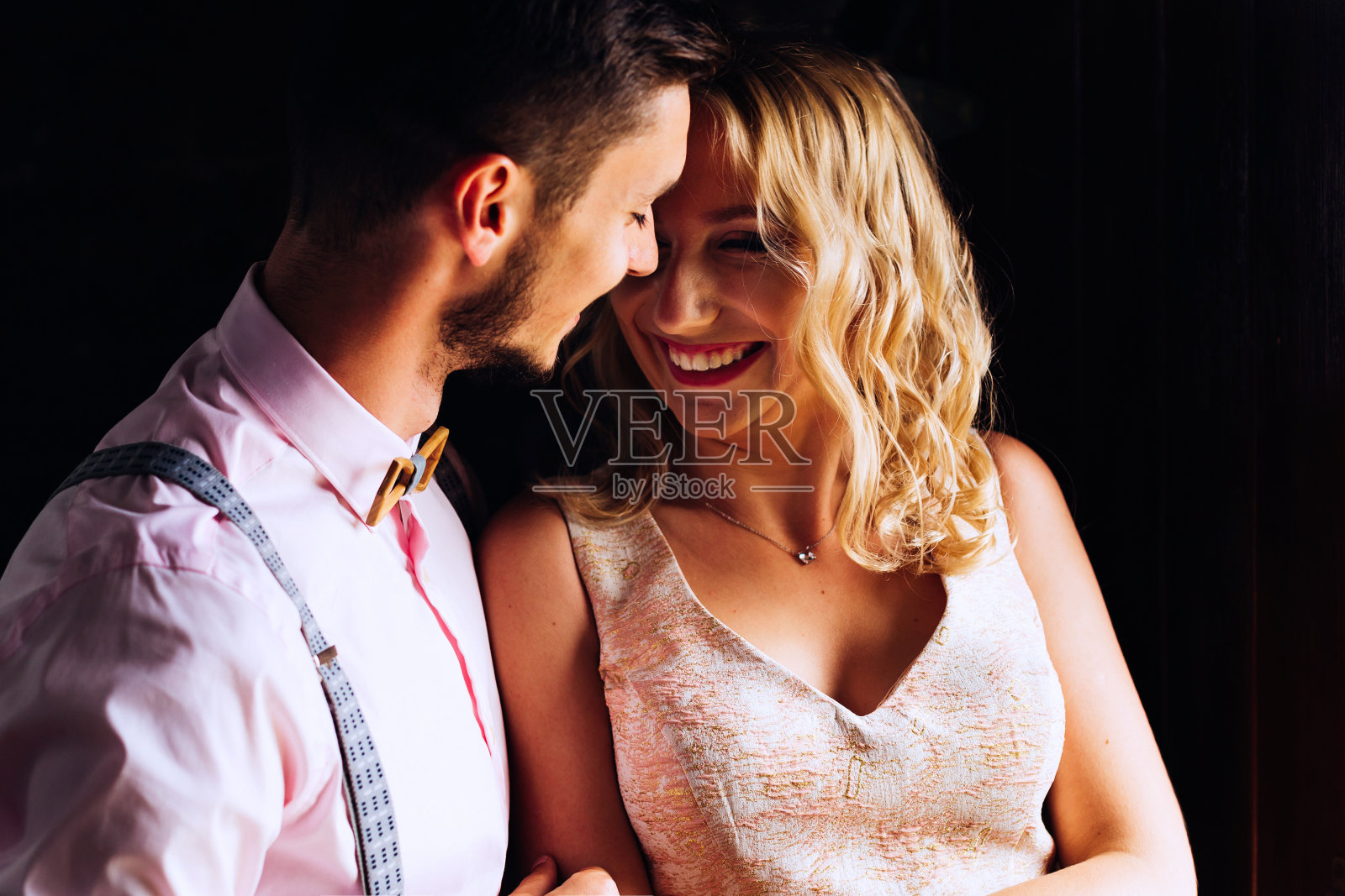 男孩温柔地拥抱着他的女朋友，她对着黑暗的背景真诚地笑了起来照片摄影图片