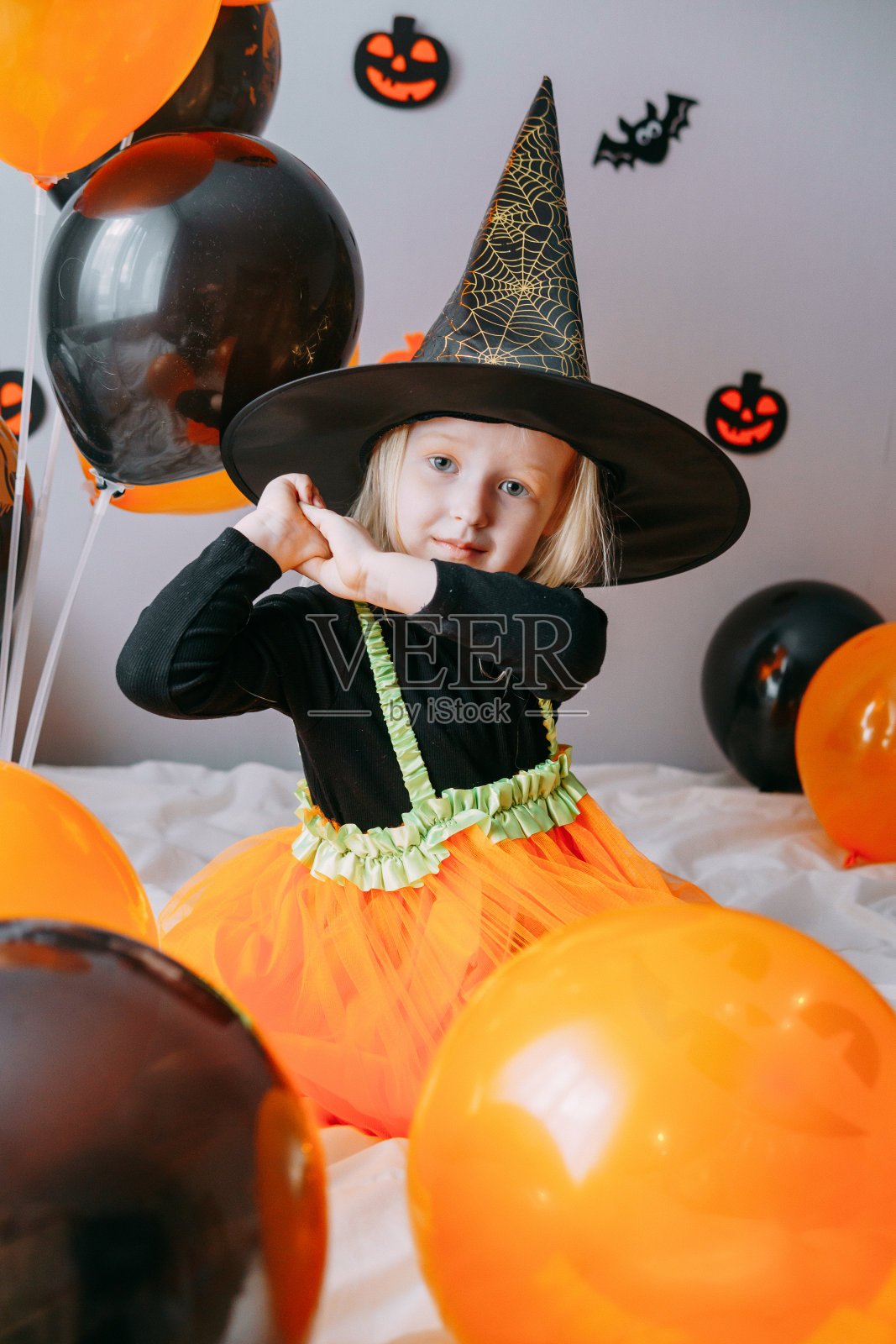 孩子们的万圣节——一个戴着女巫帽和狂欢节服装的女孩，在家里放着橙色和黑色的气球。准备好庆祝万圣节了照片摄影图片