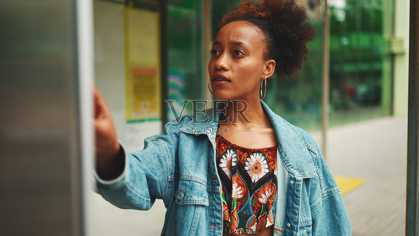 可爱的非洲女孩扎着马尾，穿着牛仔夹克，穿着民族图案的露脐上衣，站在公交车站微笑照片摄影图片