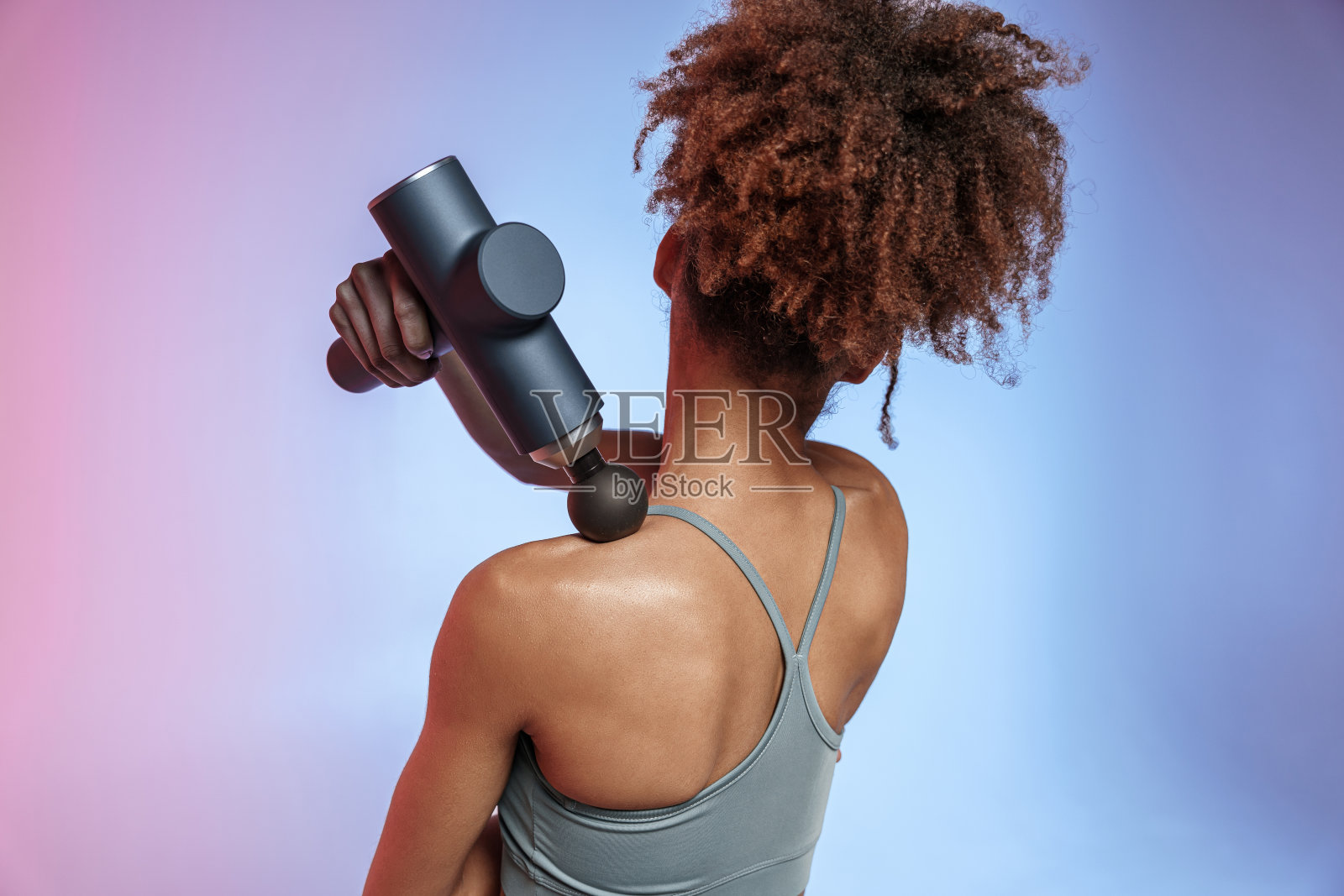 背部观点的妇女使用按摩枪机康复后，肌肉锻炼站在工作室背景照片摄影图片