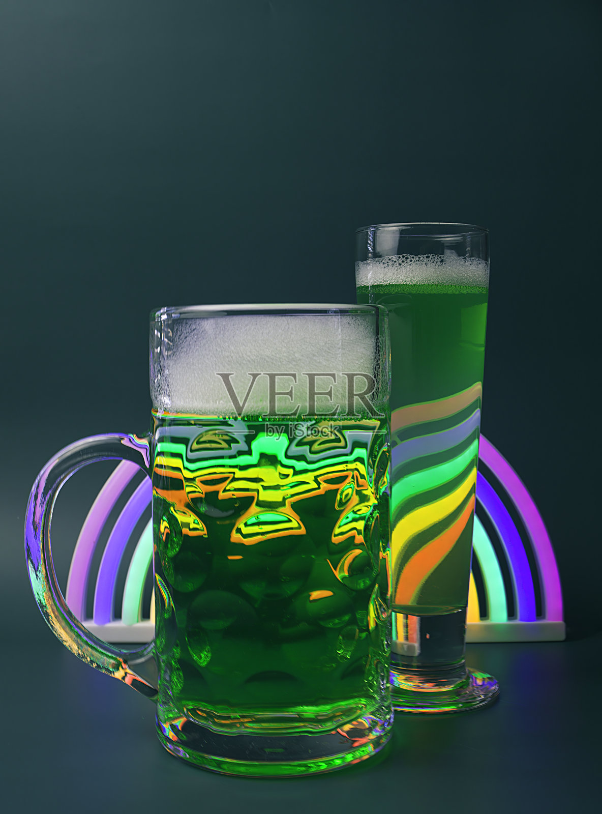 一品脱圣帕特里克节的欢呼-一杯泡沫绿色啤酒，皮尔森啤酒和霓虹灯彩虹在绿色背景照片摄影图片