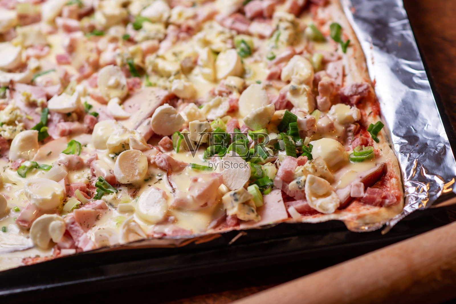 在烤盘上做自制披萨。披萨配马苏里拉芝士，香草和火腿。照片摄影图片