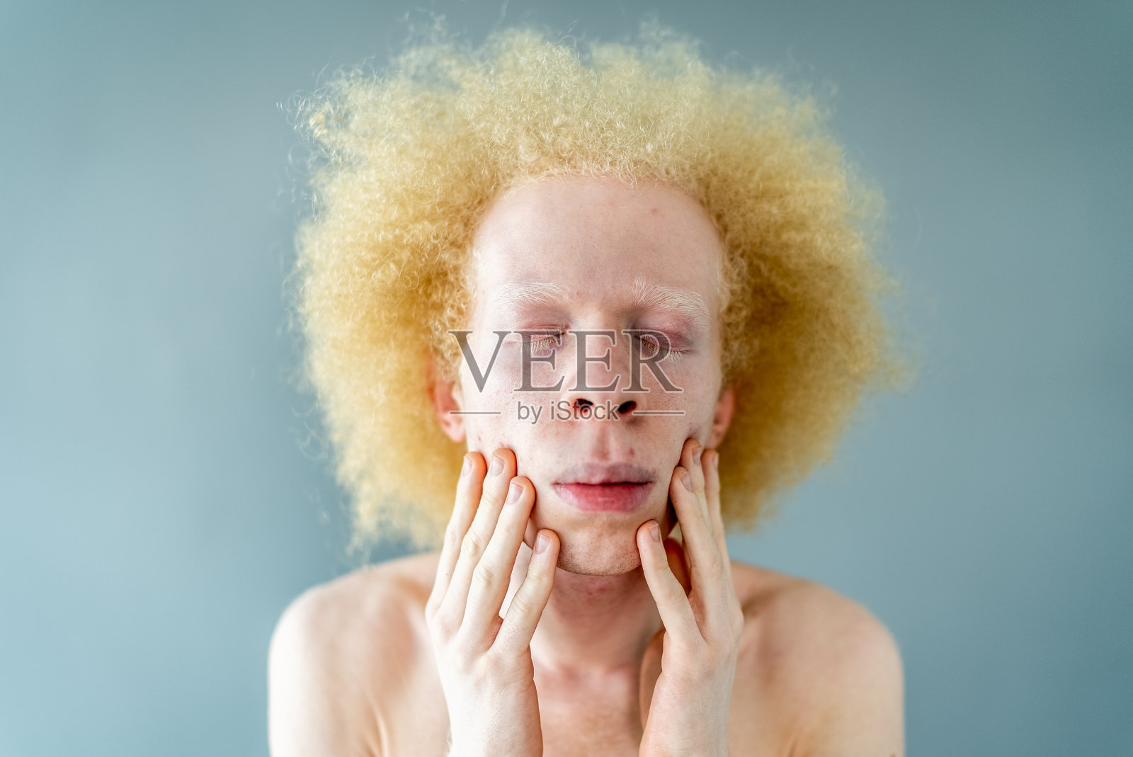 年轻男子双手放在脸颊上，闭着眼睛在工作室拍摄照片摄影图片