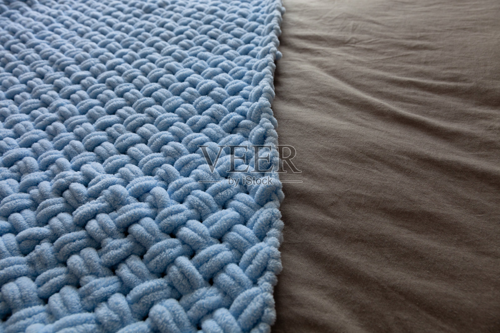 米色床单上的蓝色柔软针织毛毯照片摄影图片