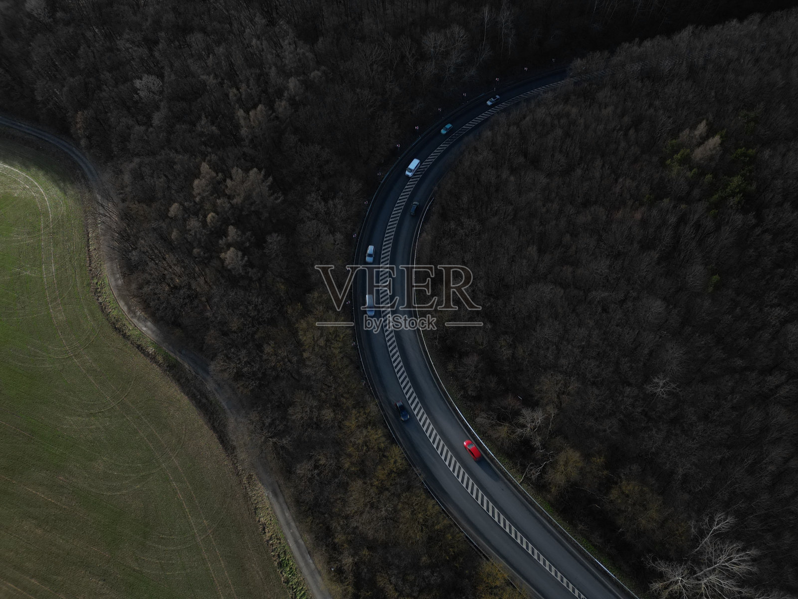 鸟瞰一条宽阔的道路，蜿蜒在荒野中被深色树木覆盖的小山周围照片摄影图片