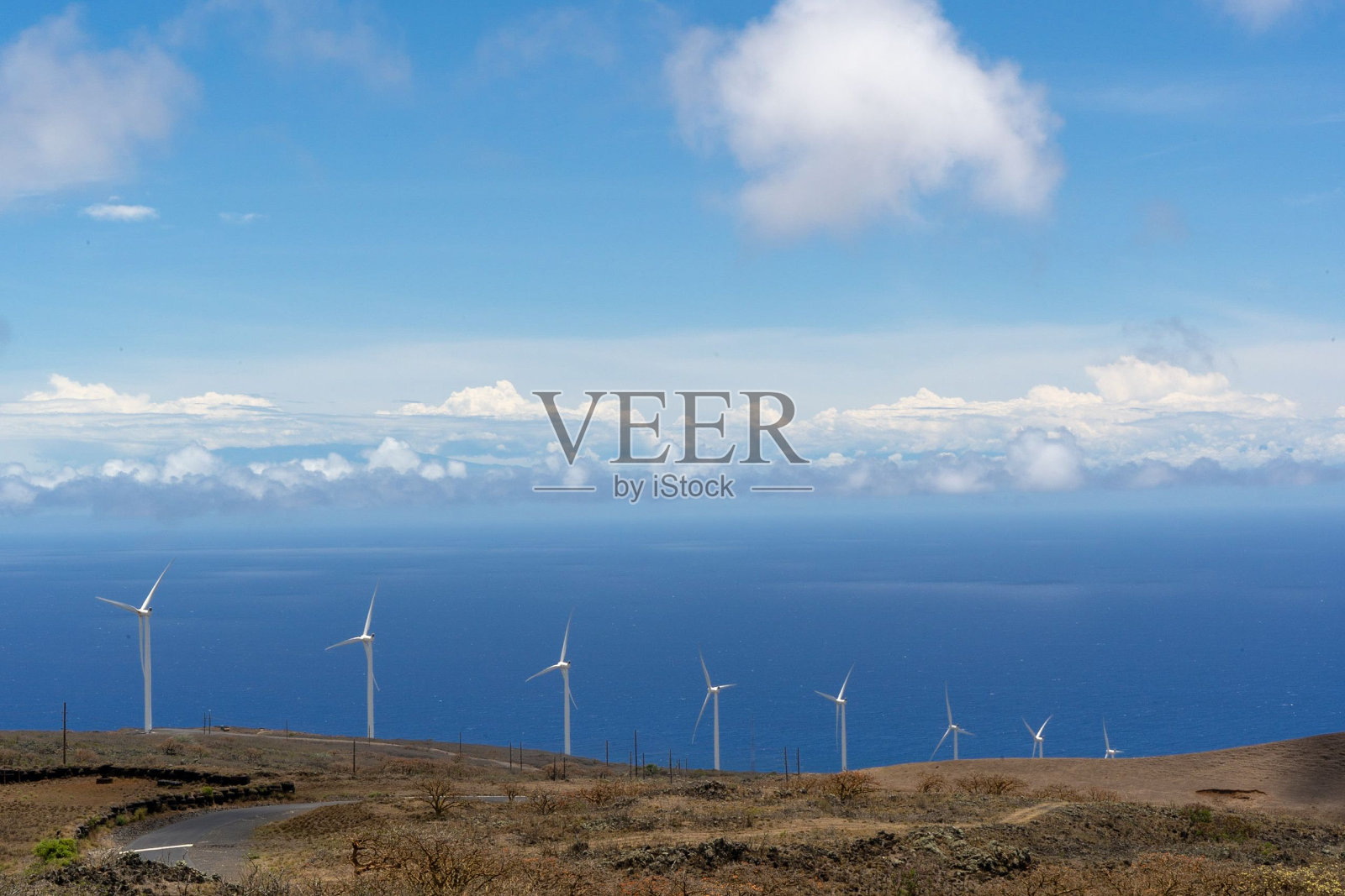 风轮机在海边的小山上，蓝天白云下。照片摄影图片