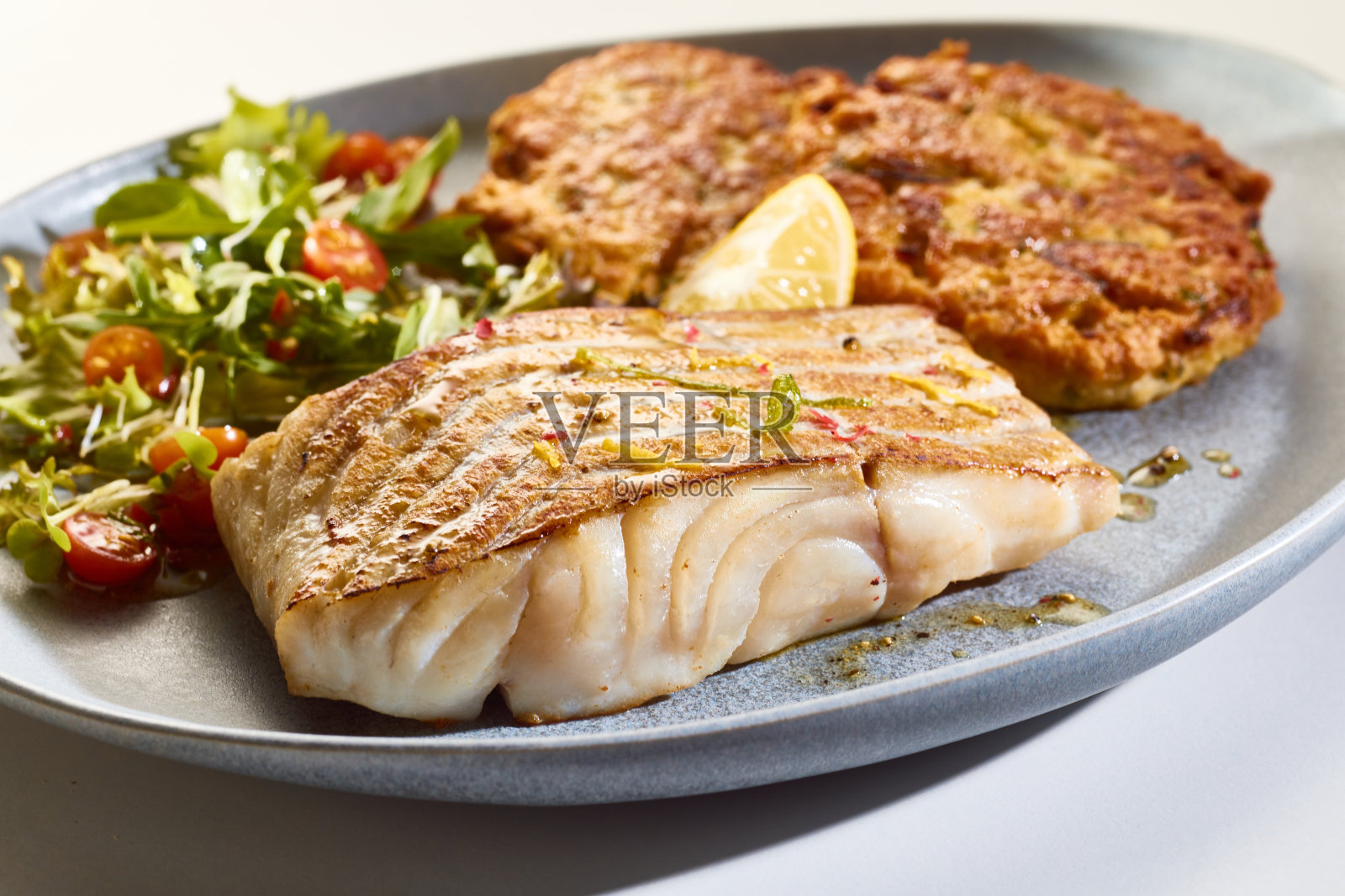 开胃的鱼片配蔬菜沙拉和肉排，盛在盘子里照片摄影图片