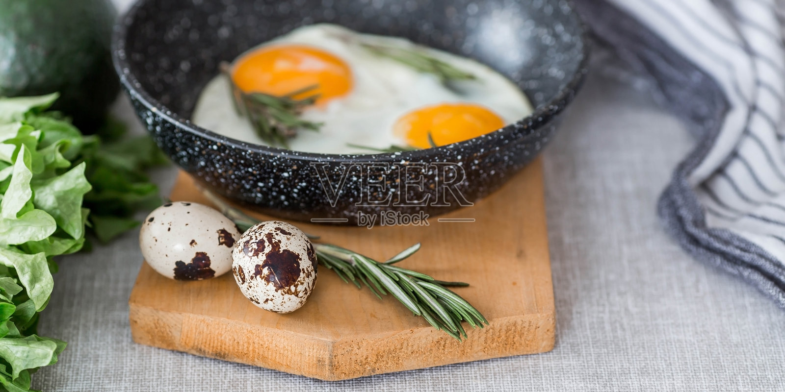 在平底锅里煎蛋，配上迷迭香、面包、鸡蛋和蔬菜沙拉，铺在亚麻桌布上。早餐，午餐和晚餐。视图是软的，选择性聚焦。乡村风格。照片摄影图片