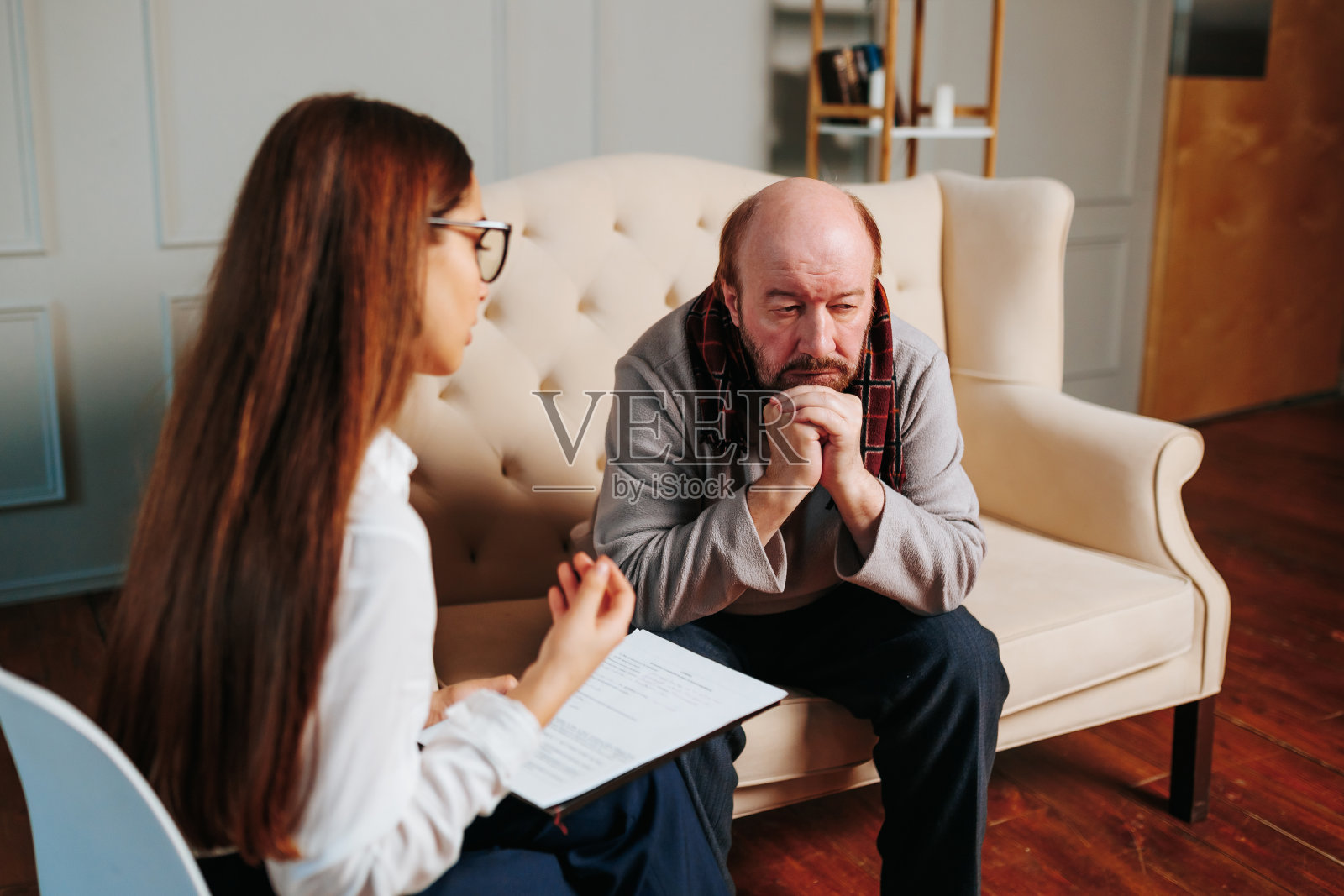 一个秃顶的老男人看着一个年轻的护士。成熟的女心理医生与悲伤沟通照片摄影图片