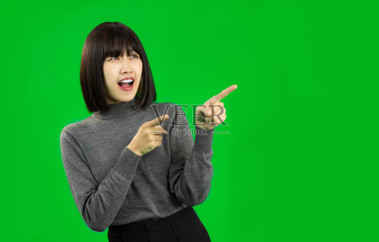 年轻的亚洲女人穿着灰色衬衫指着绿色屏幕上的东西。照片摄影图片