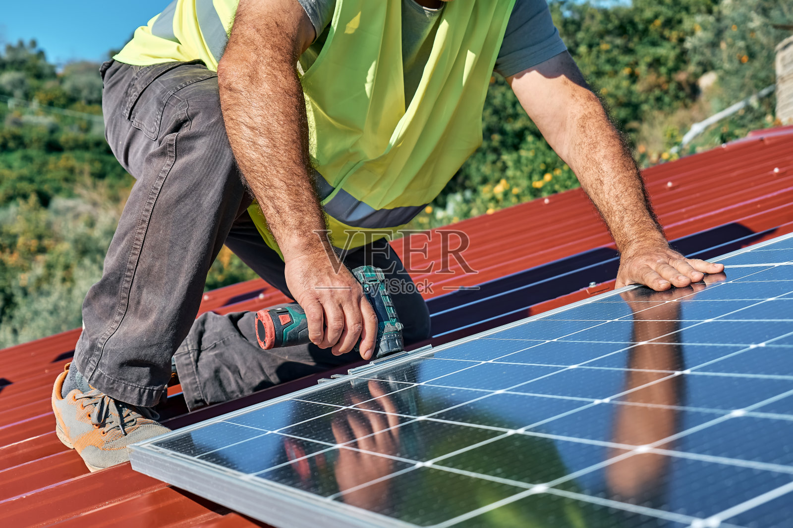 男子用钻头在一所房子的屋顶上安装独立的光伏太阳能电池板系统。替代能源、可再生能源和电力可持续资源的概念。照片摄影图片