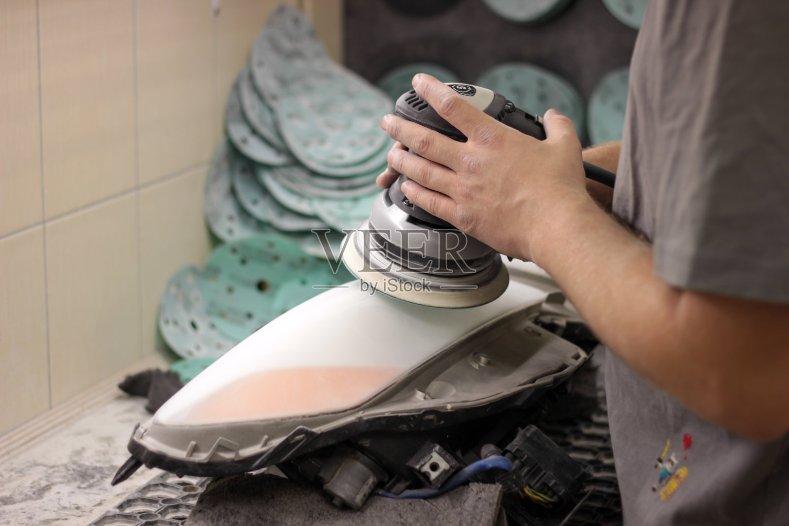 使用磨床修复大灯玻璃。一名男子在服务站用抛光机抛光汽车大灯的光学元件。用抛光机工作的手。照片摄影图片