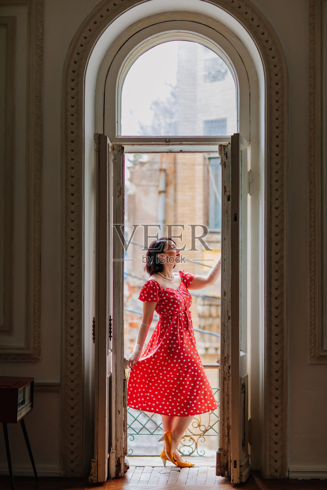 一个美丽而快乐的黑发女人在阳台门口穿着红色复古服装照片摄影图片