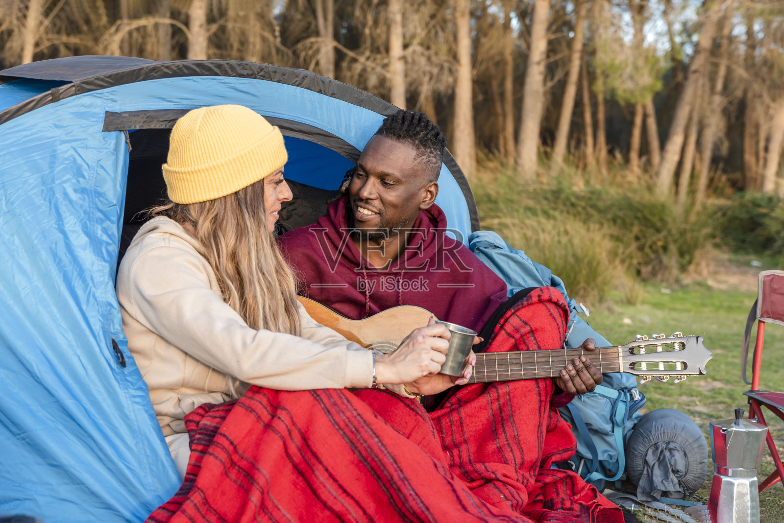 相爱的多民族情侣坐在帐篷里，看着对方，露营，弹吉他照片摄影图片
