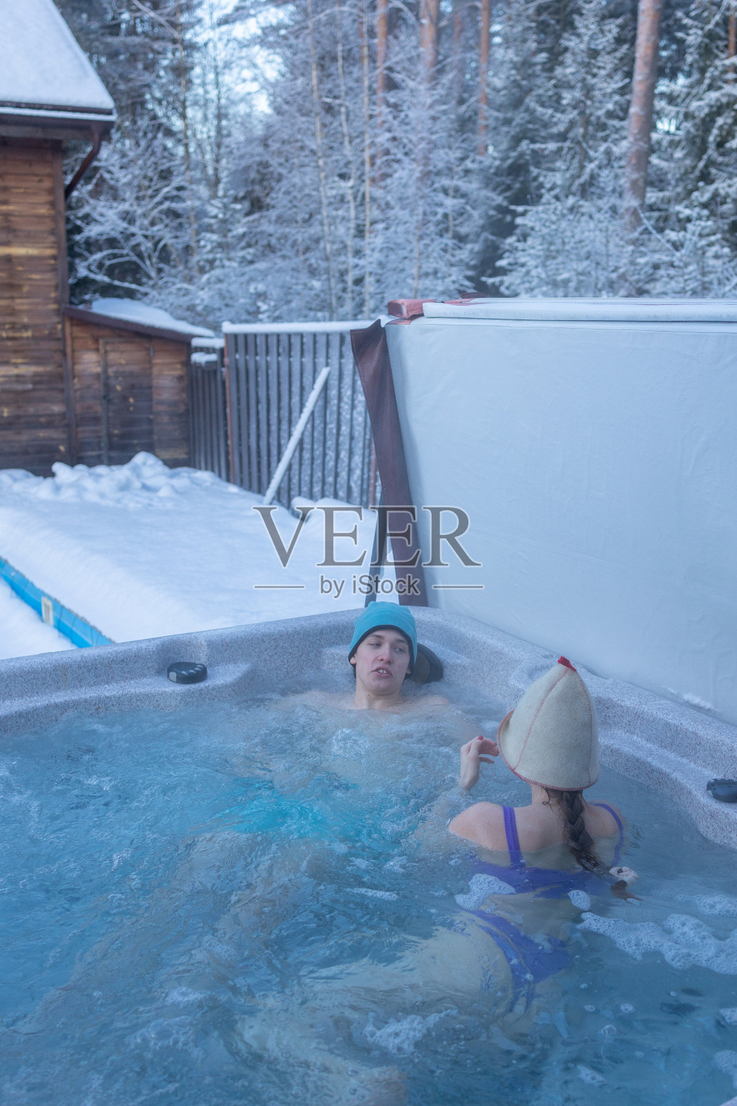 在寒冷的冬天，一群快乐的青少年在按摩浴缸里享受着热水浴。在大自然的户外热水浴缸里无忧无虑地放松。与朋友见面聊天照片摄影图片