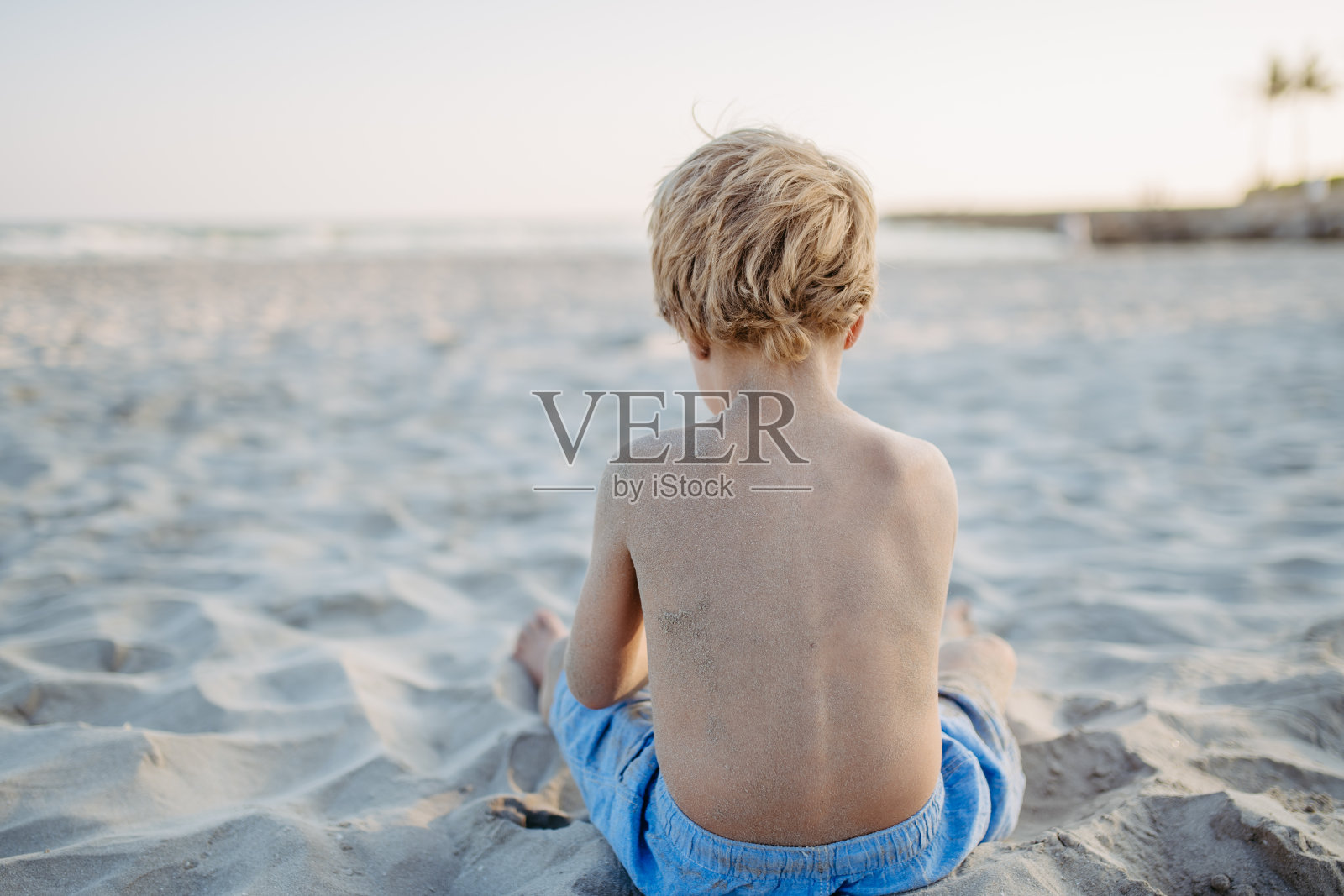 小男孩在沙滩上玩耍，后视图。照片摄影图片