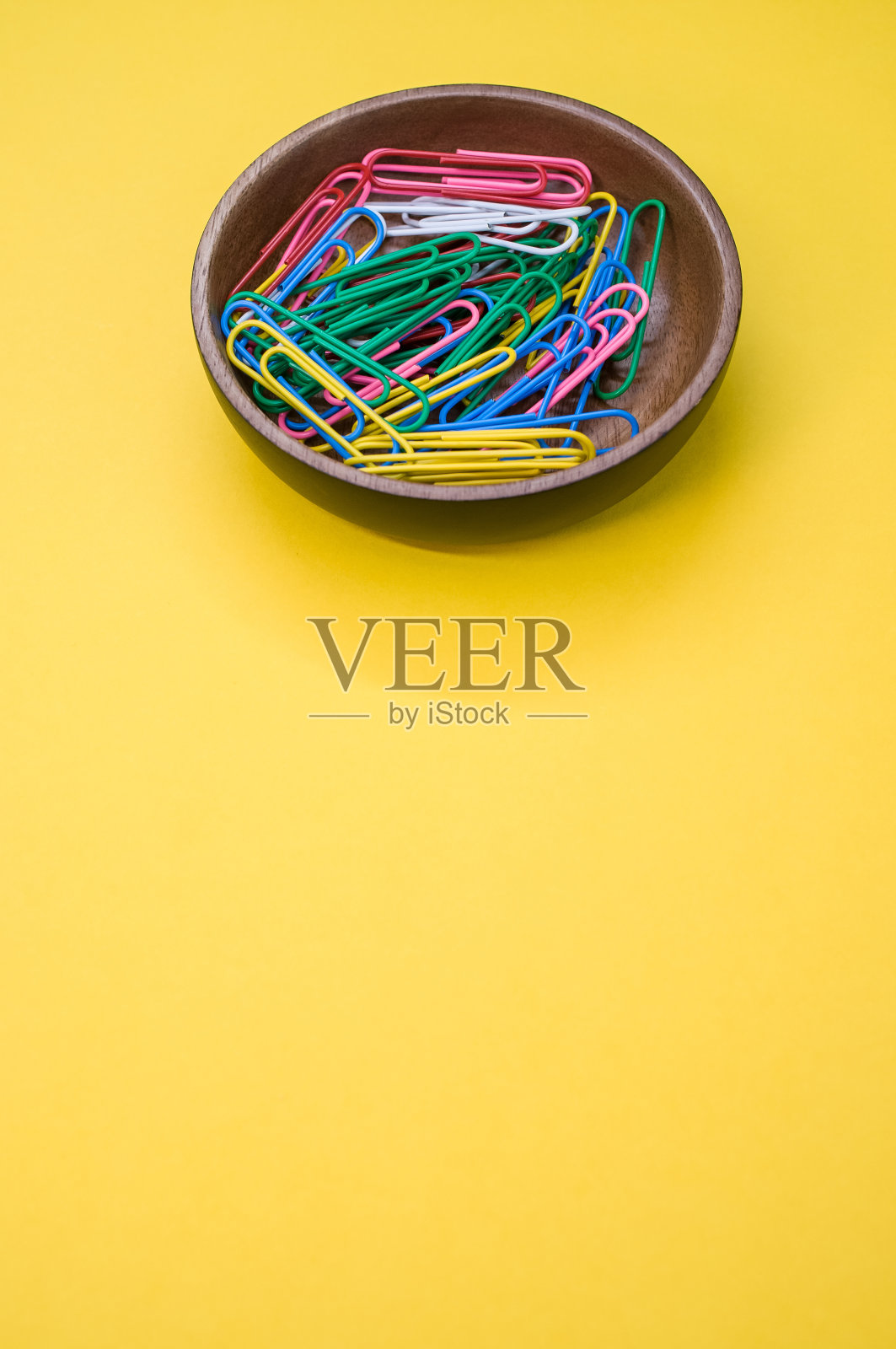 垂直拍摄彩色回形针在一个木碗上的黄色背景照片摄影图片
