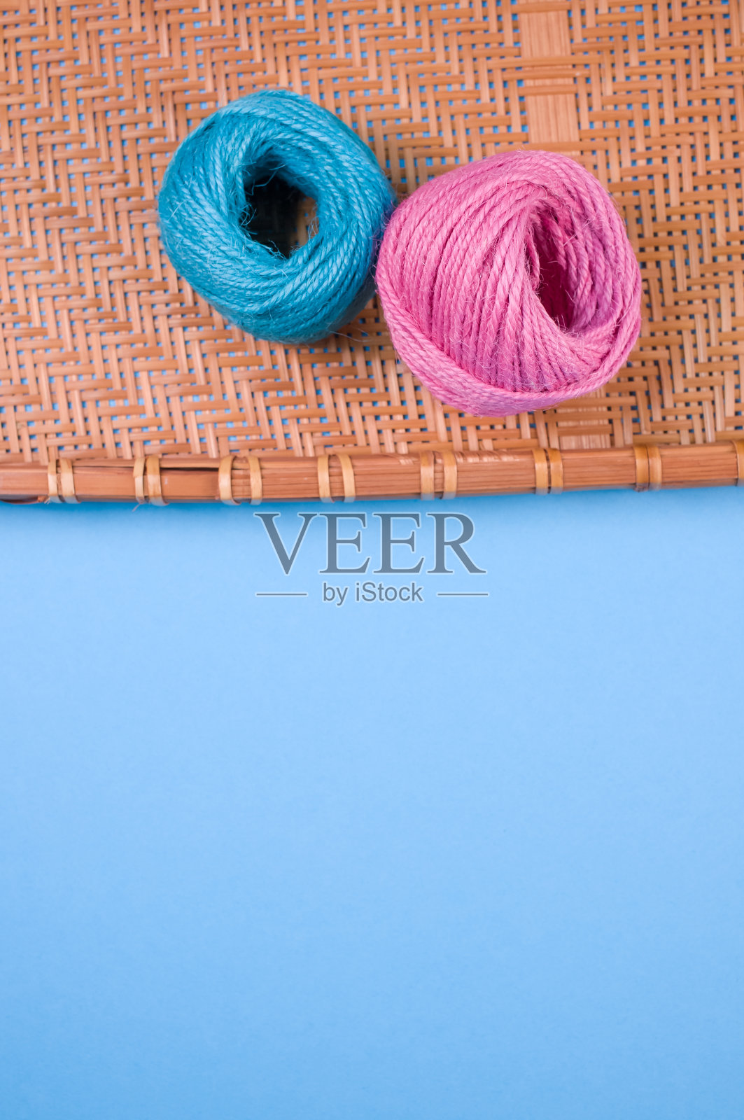 垂直拍摄的蓝色和粉色纱线在竹柳条托盘隔离在蓝色背景照片摄影图片