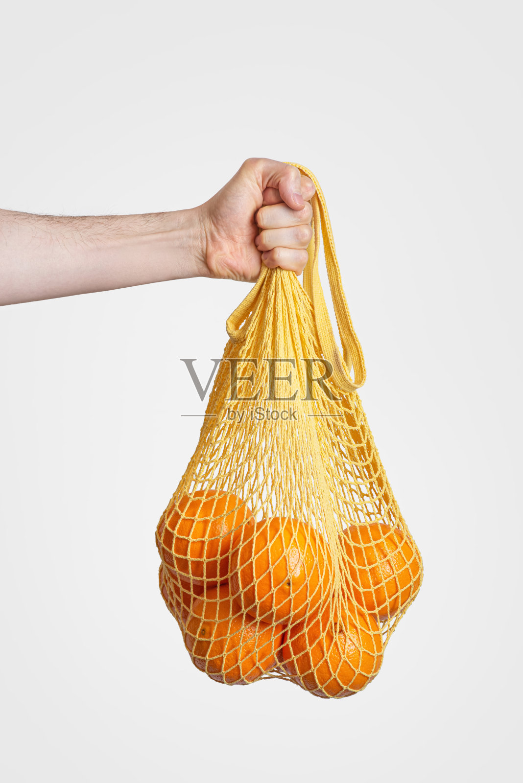 零废物包装。灰色背景下，一个男人手里拿着橘子的购物袋照片摄影图片