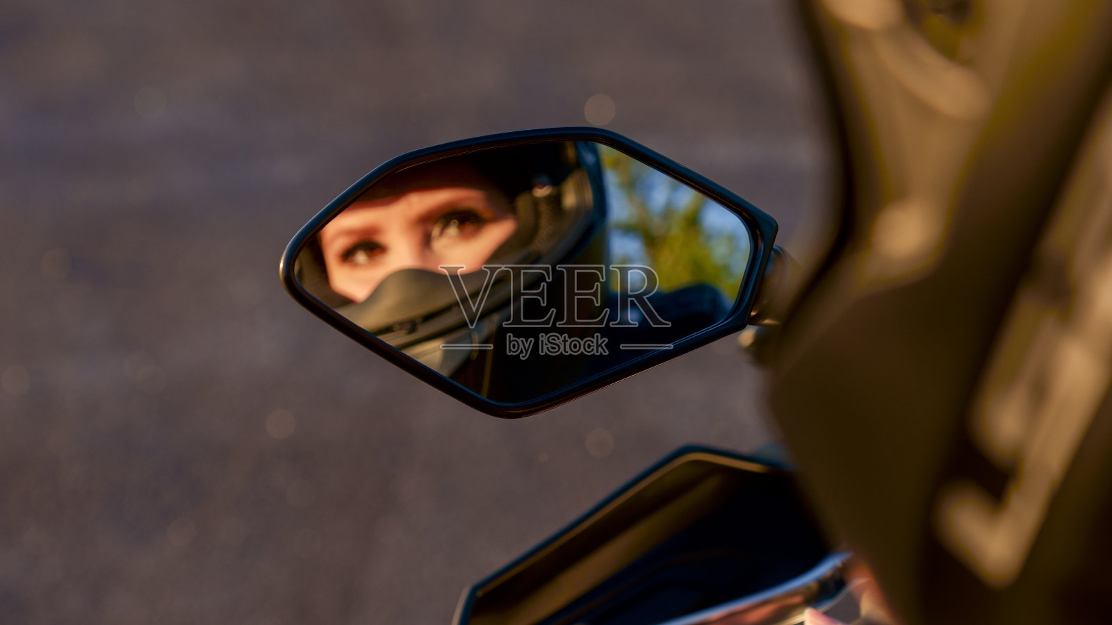 骑摩托车的女孩。镜子里模糊的倒影。有选择性的重点。在摩托车的镜子里展示女孩。非常漂亮的眼睛。照片摄影图片