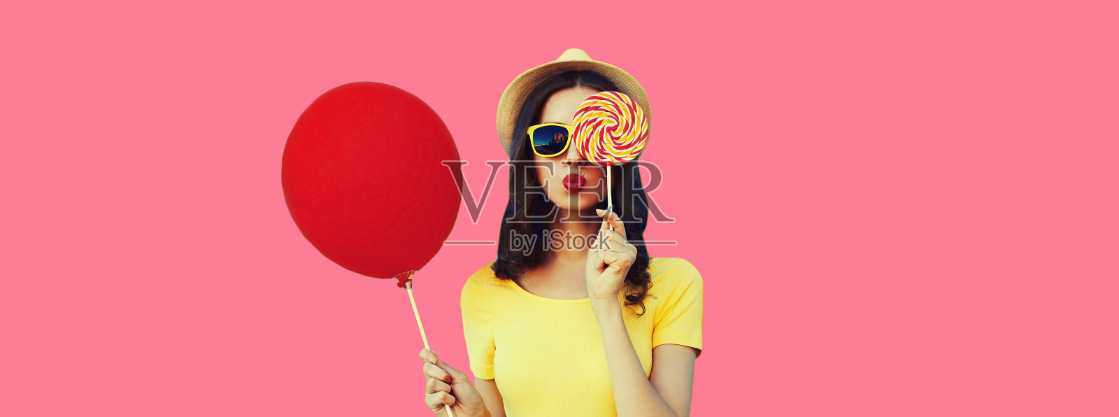 美丽的年轻女子在粉红色背景上用棒棒糖和红色气球遮住她的眼睛照片摄影图片