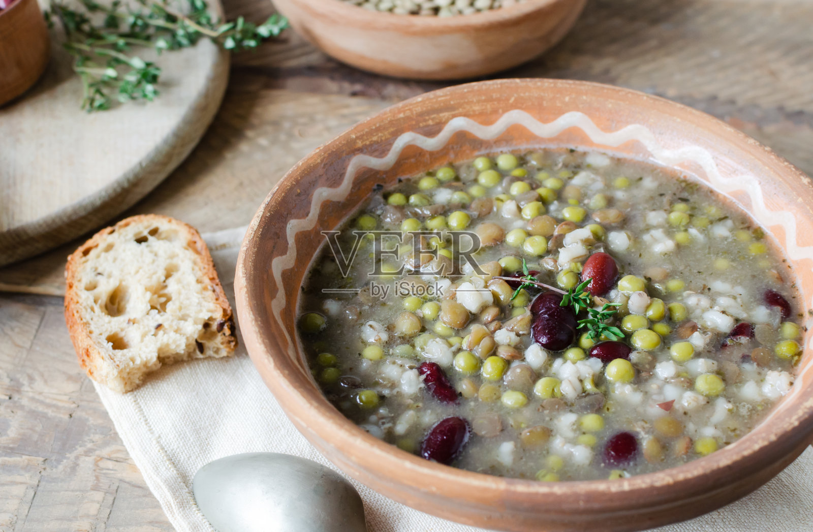 瓷碗里盛着豆汤，木桌上放着一小枝百里香和一片面包。红豆、扁豆和豌豆的混合物。素食的概念。乡村风格。水平方向。照片摄影图片