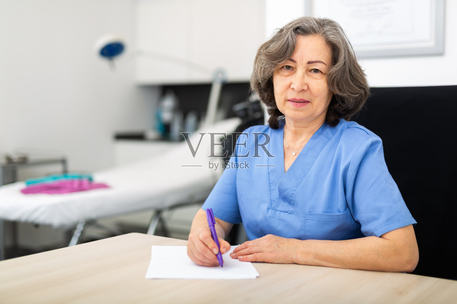 有经验的医生坐在柜子的工作桌前写重要的笔记照片摄影图片