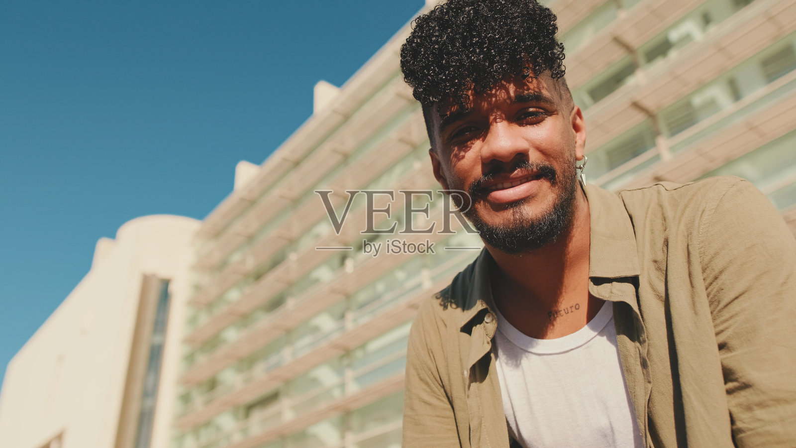 穿着橄榄色衬衫的年轻男学生坐在大学旁边的外面照片摄影图片