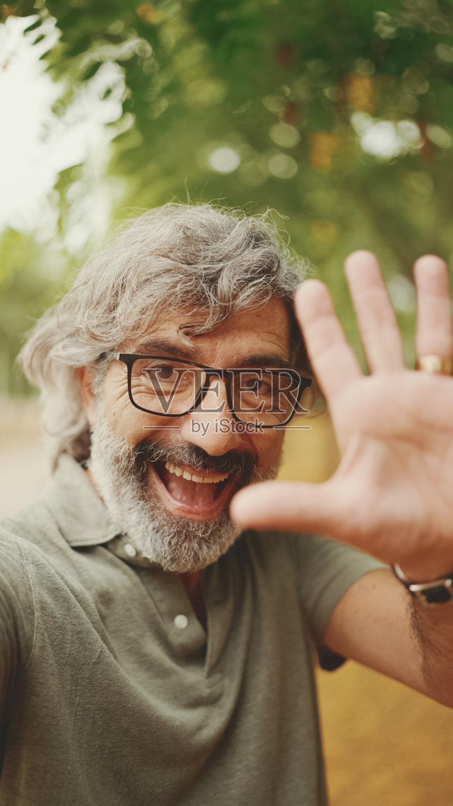 友好的中年男子，灰色头发和胡子，穿着便装，正在使用手机。成熟的绅士戴着眼镜自拍，用手机视频通话照片摄影图片