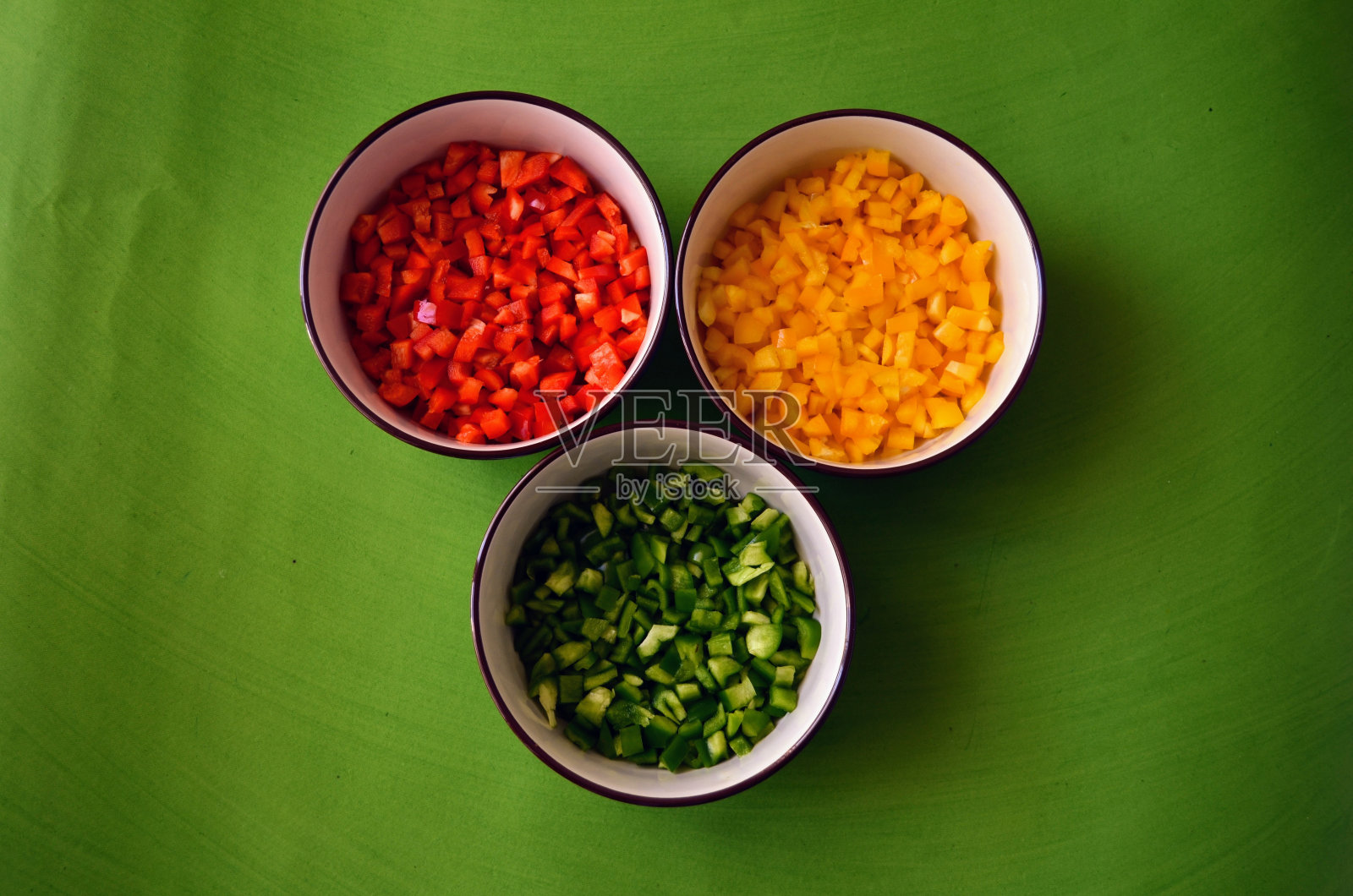 青椒、红椒、黄椒切丁，放在三个不同的碗里，味道和营养价值各不相同。新鲜蔬菜。准备在食谱中使用。绿色背景。照片摄影图片