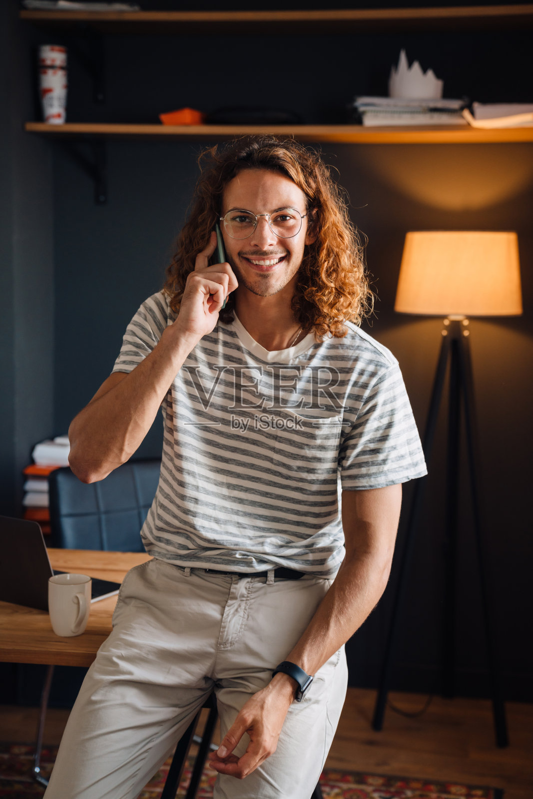 年轻的卷毛男子在办公室喝咖啡和打电话照片摄影图片