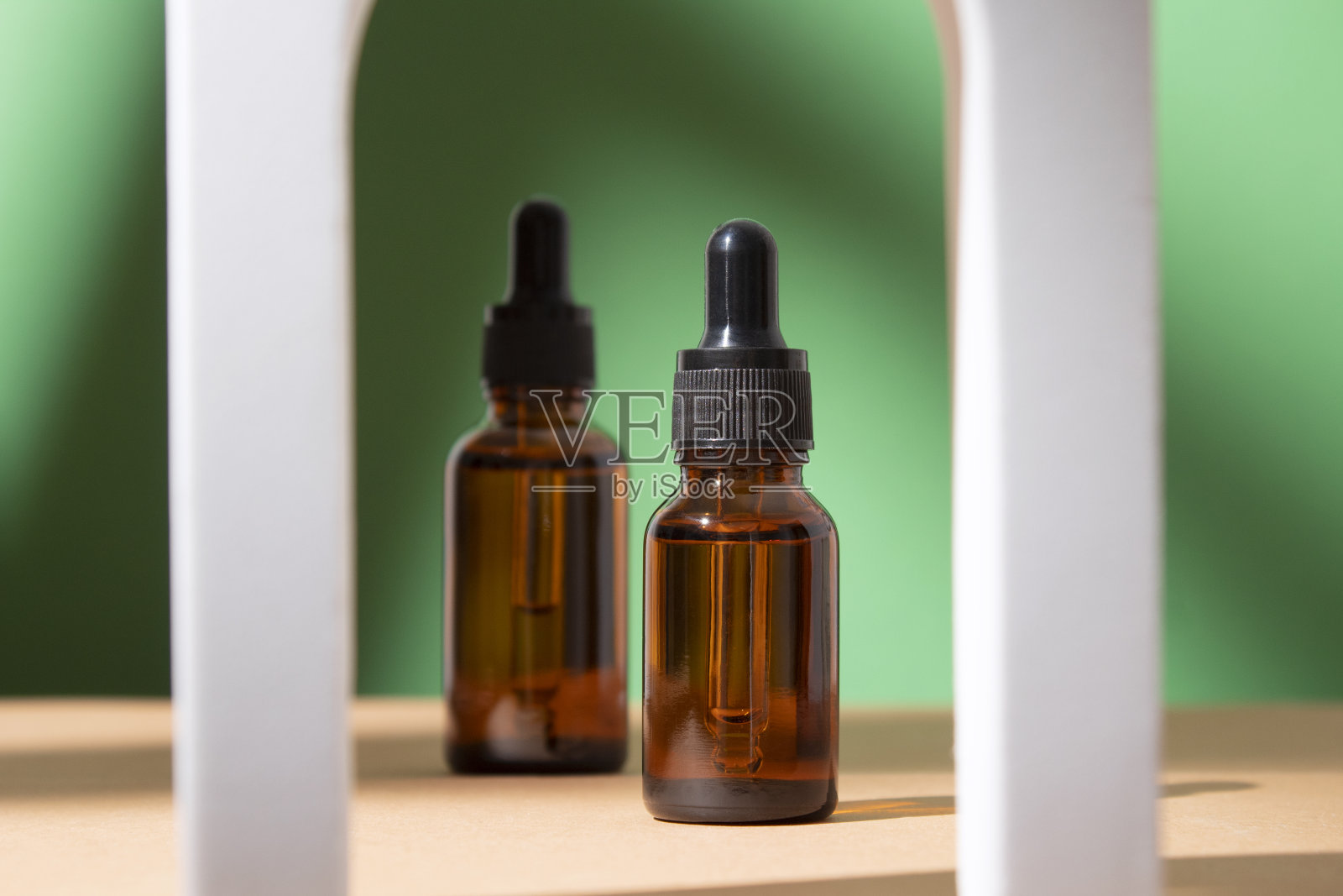 美容胶原蛋白面部血清在一个玻璃滴管瓶在拱门上的绿色背景。化妆品包装的潮流拍摄。天然成分的精油。照片摄影图片