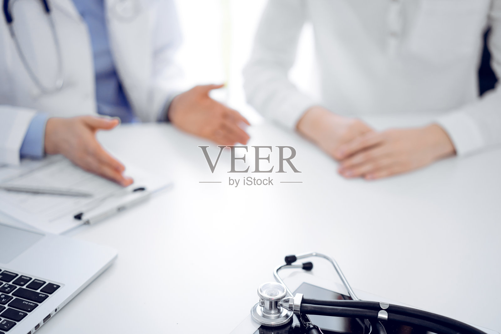 听诊器放在平板电脑上，医生和病人坐在一起。医学、保健概念照片摄影图片